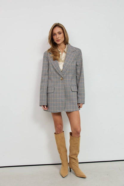 Woman wearing a gray checkered blazer dress with beige knee-high boots against a white background