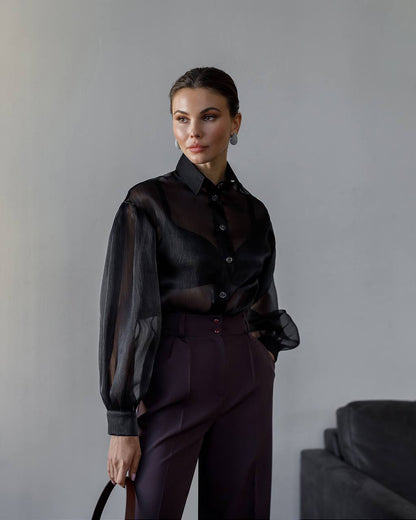 Woman wearing a black blouse and dark pants against a gray background