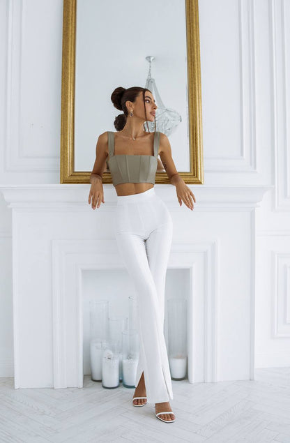 Woman in a green top and white pants standing in a room with a mirror and decorative items.