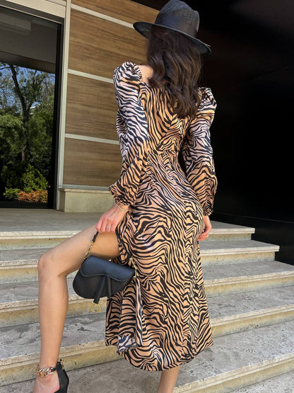 Person wearing a zebra print dress and black hat on steps outside a building.