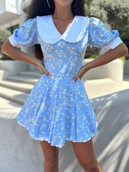 Woman wearing a blue floral dress with white accents outdoors.
