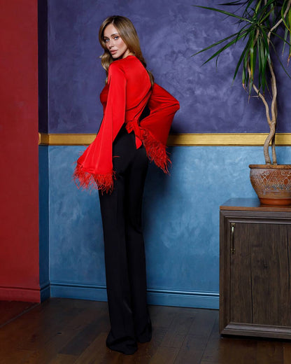 Woman in a red top and black pants standing against a blue wall with a plant on a wooden cabinet.