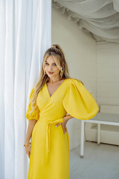 Woman wearing a yellow dress with puffed sleeves in a bright room.
