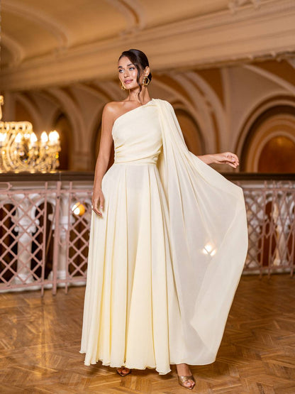 Woman in a flowing white dress standing in an elegant indoor setting with chandeliers.
