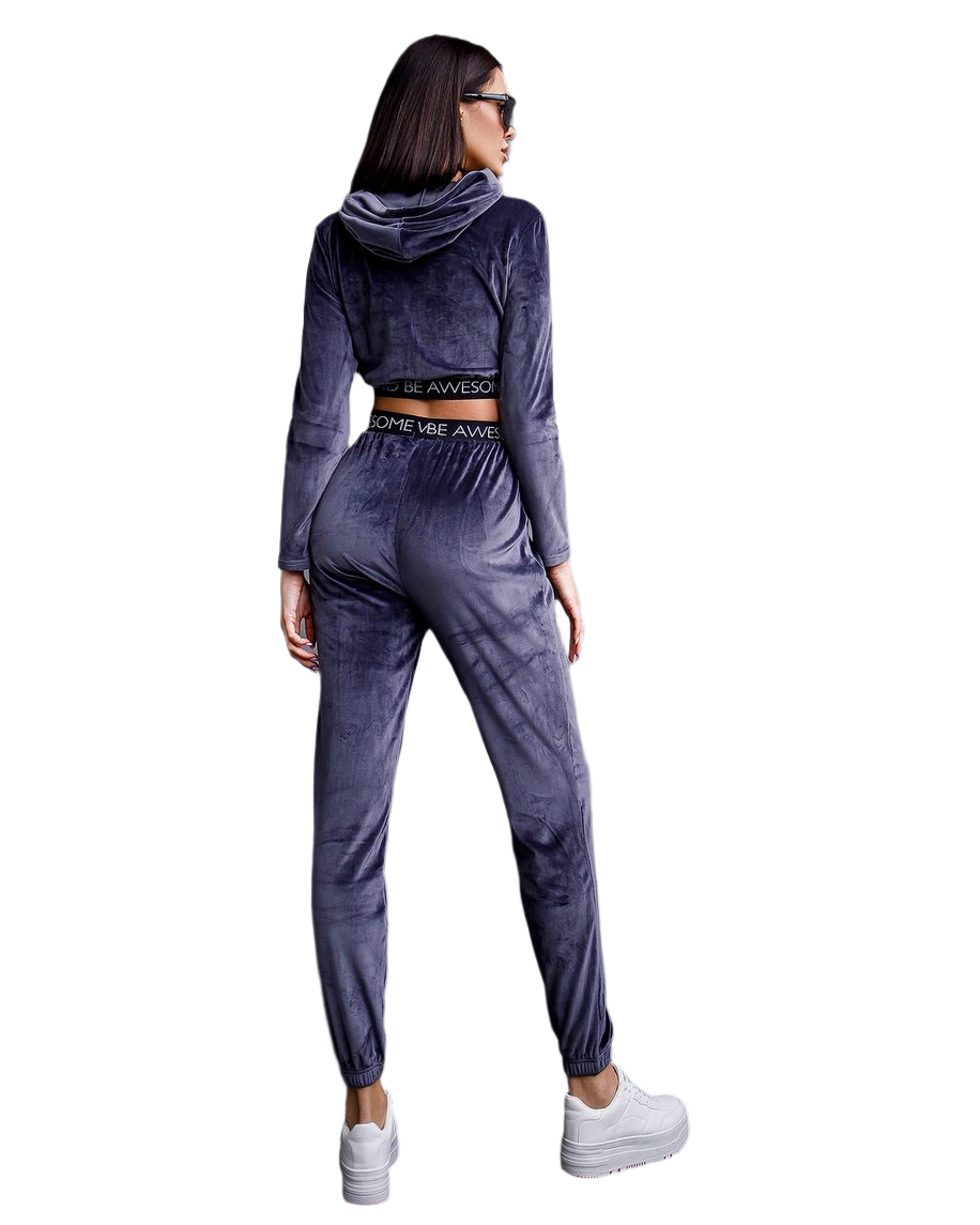 Woman wearing a gray velour tracksuit with white sneakers on a white background