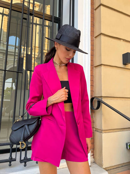 Woman in a bright pink suit and black hat standing outside a building.