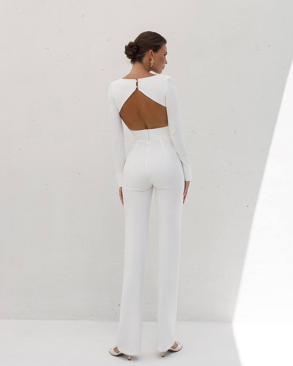 Woman wearing a white jumpsuit with a cutout back design on a plain background