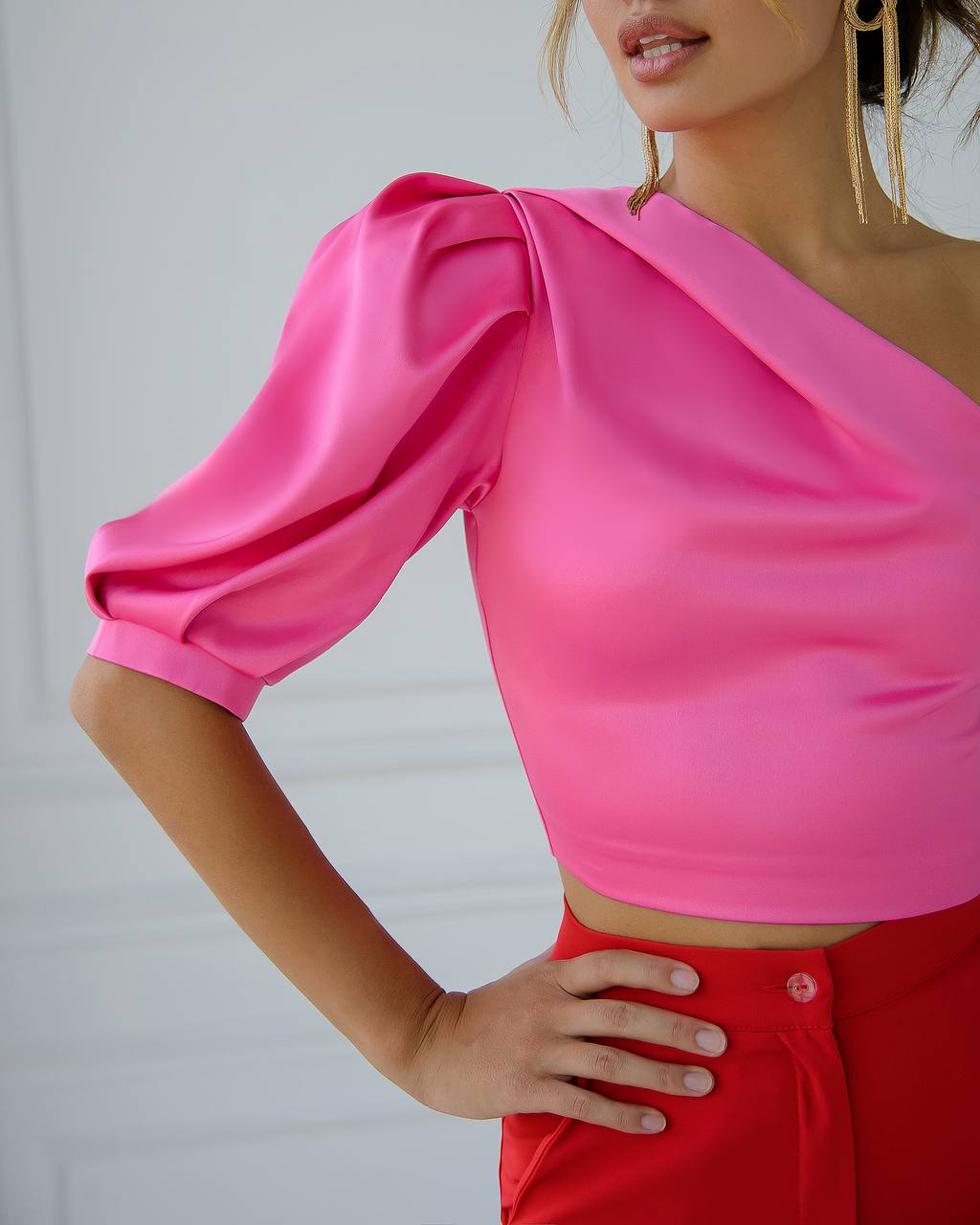 Person wearing a bright pink one-shoulder top with puffed sleeves against a white background