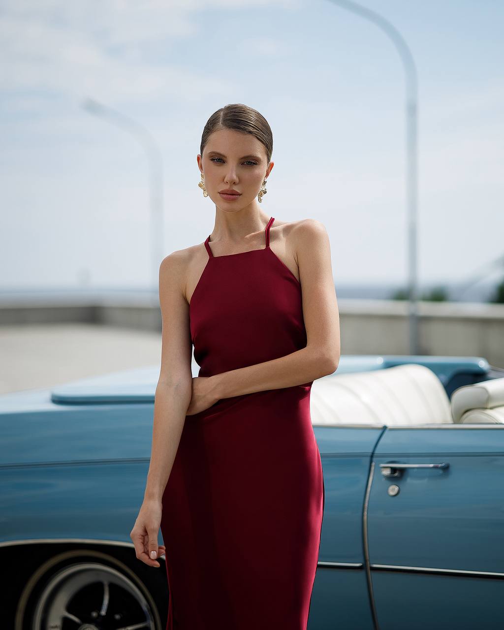 Woman in a burgundy dress standing next to a vintage blue car with a blurred background