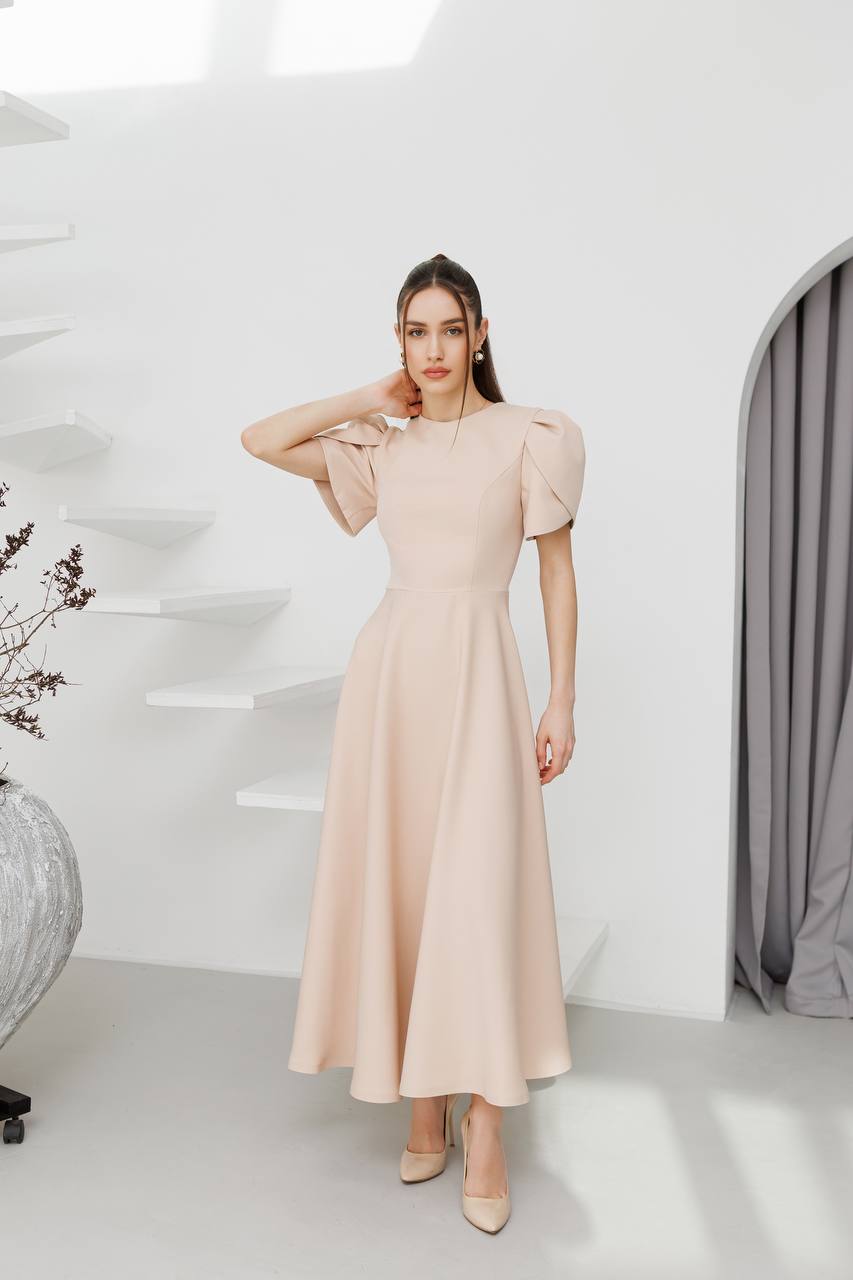 Woman wearing a beige dress with puffed sleeves in a minimalistic room.