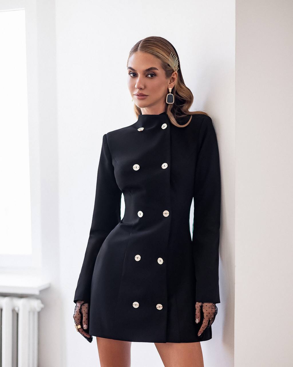 Woman wearing a black dress with white buttons against a white wall
