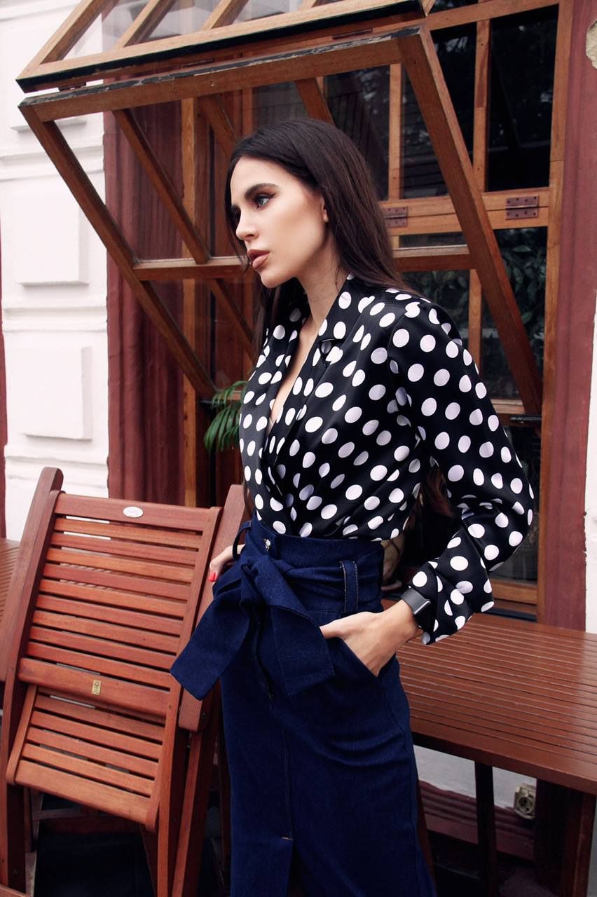 Woman wearing a black and white polka dot blouse with a navy skirt outdoors.