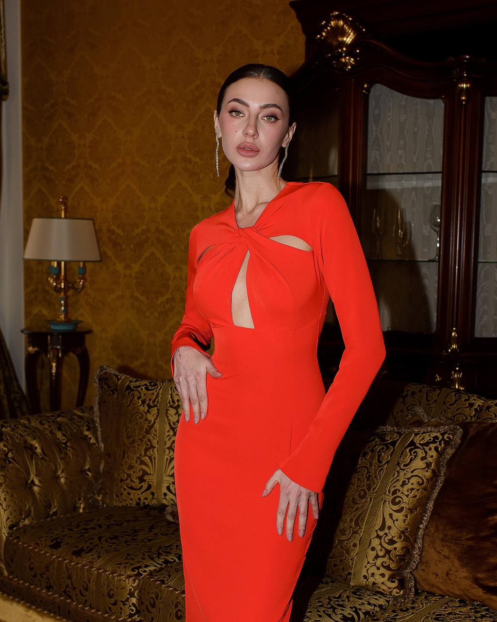 Woman in a red dress standing in an ornate room with gold accents.