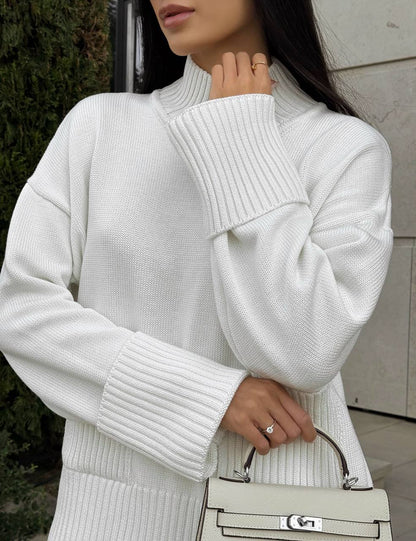 Person wearing a white ribbed sweater holding a matching handbag.