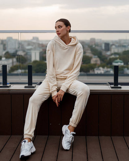 Woman in a beige tracksuit sitting on a rooftop with a cityscape in the background