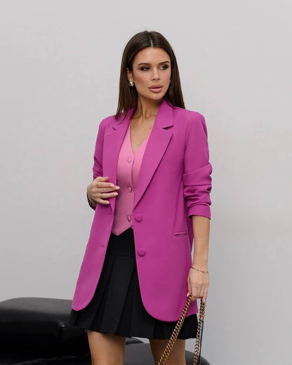 Woman wearing a bright pink blazer over a pink top and black skirt on a gray background