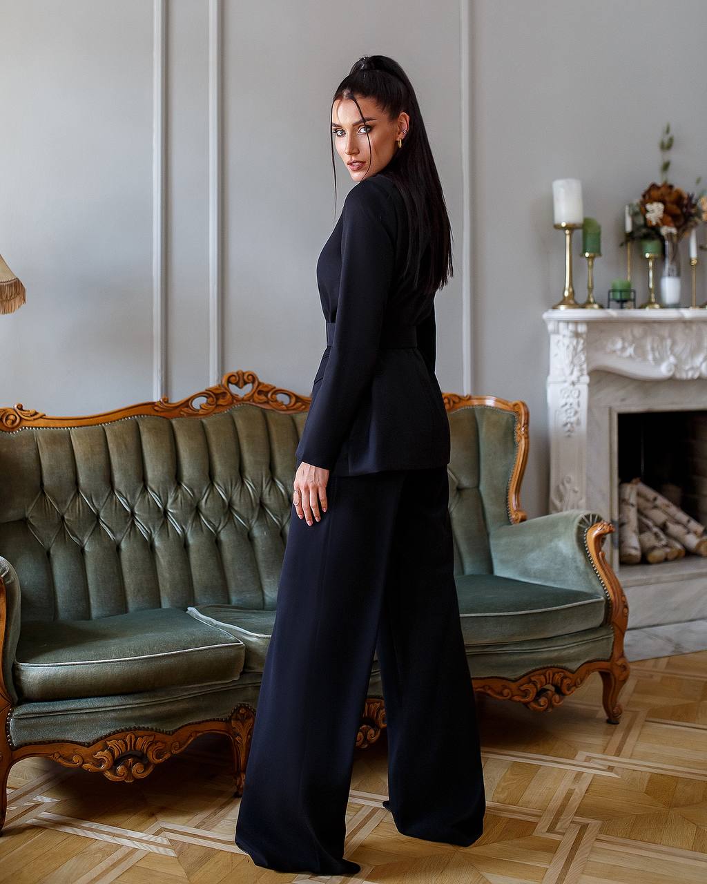 Woman in a black outfit standing in a stylish room with a sofa and fireplace.