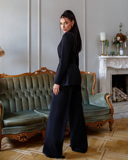 Woman in a black outfit standing in a stylish room with a sofa and fireplace.