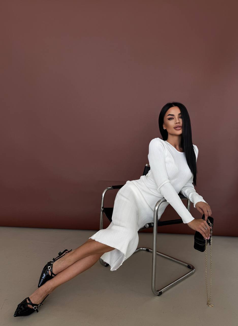 Woman in a white outfit sitting on a chair against a brown background