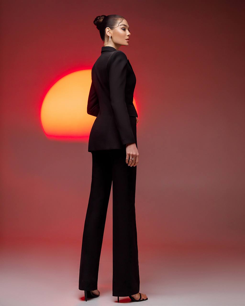 Woman in a black suit standing against a red sunset background