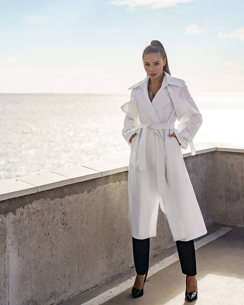 Woman wearing a white trench coat on a rooftop with a cityscape background
