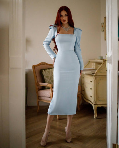 Woman in a light blue dress standing in an elegant room with wooden furniture.