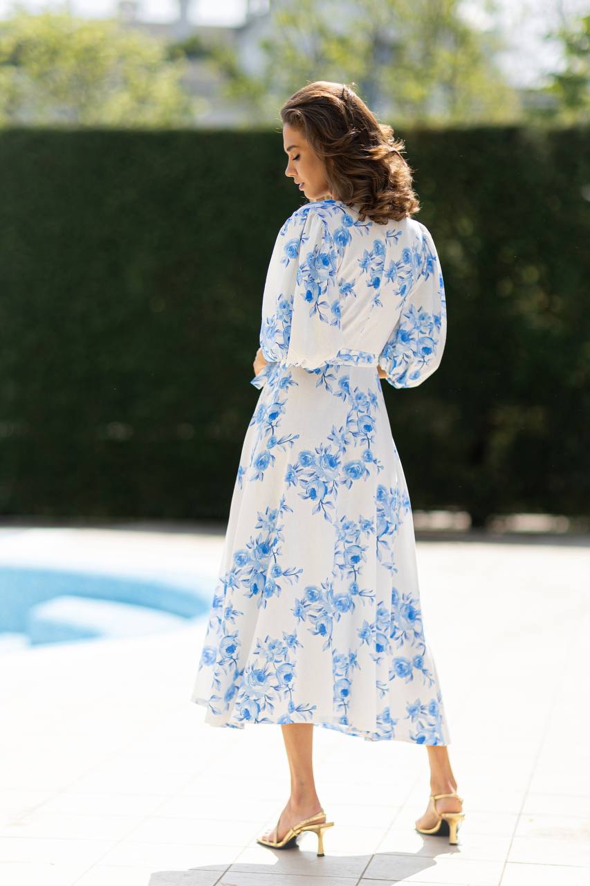 Woman in a white dress with blue floral pattern standing by a poolside.