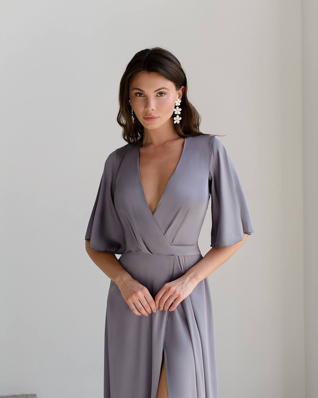 Woman wearing a gray dress with cape sleeves against a plain background