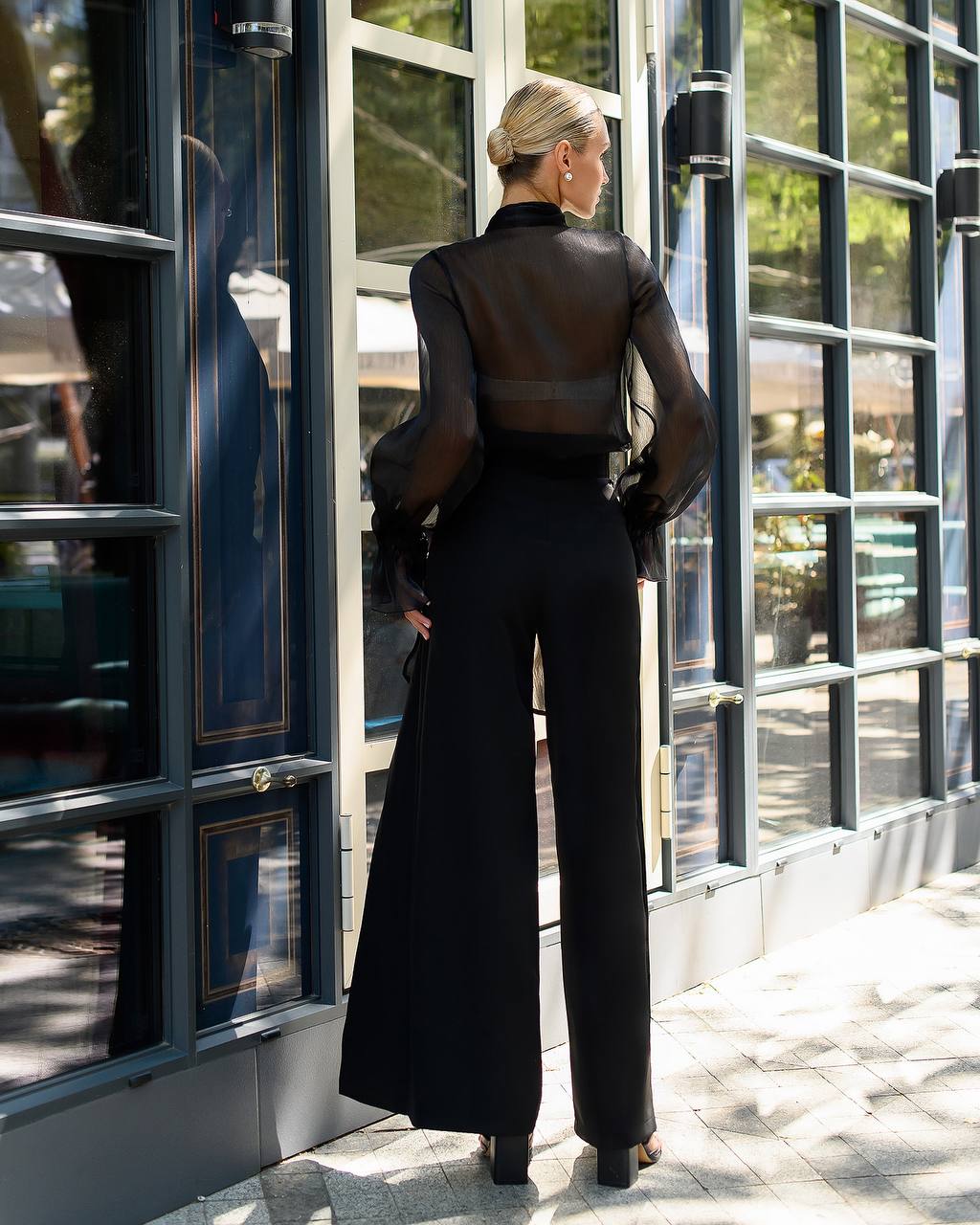 Woman in a black outfit standing in front of a modern building with large glass windows.