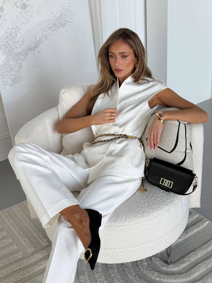 Woman in a white outfit sitting on a chair with a black handbag.