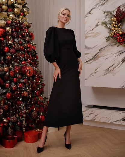 Woman in a black dress standing next to a decorated Christmas tree indoors.