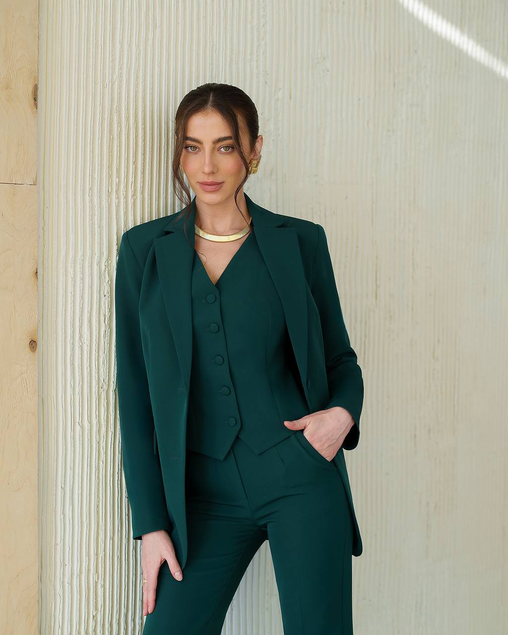 Woman wearing a green suit standing against a textured wall.