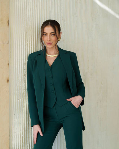 Woman wearing a green suit standing against a textured wall.
