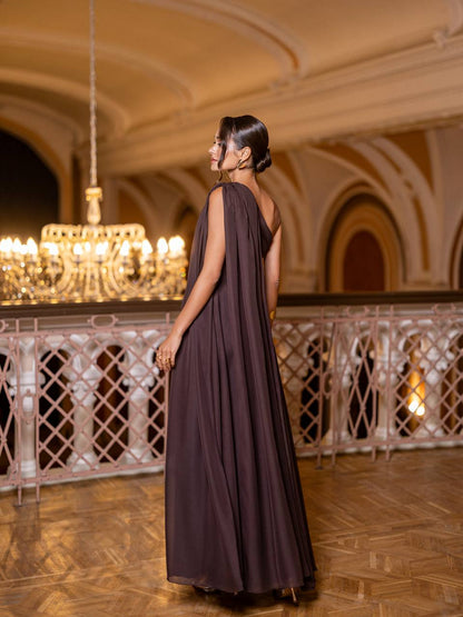 Woman in a dark purple dress standing in an elegant interior setting with chandeliers.