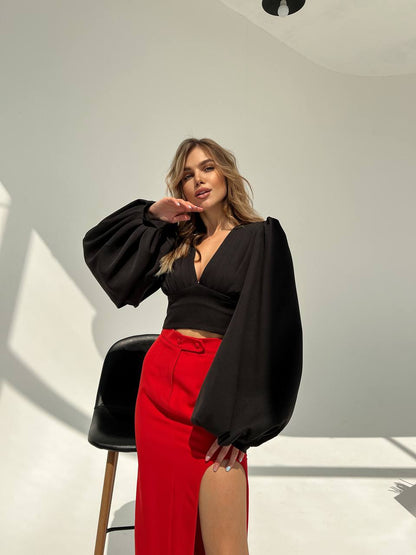 Woman wearing a black top and red pants in a minimalistic setting