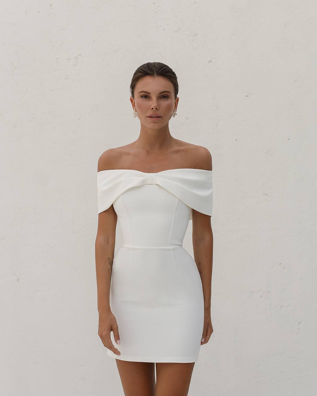 Woman wearing a white off-shoulder dress against a plain background