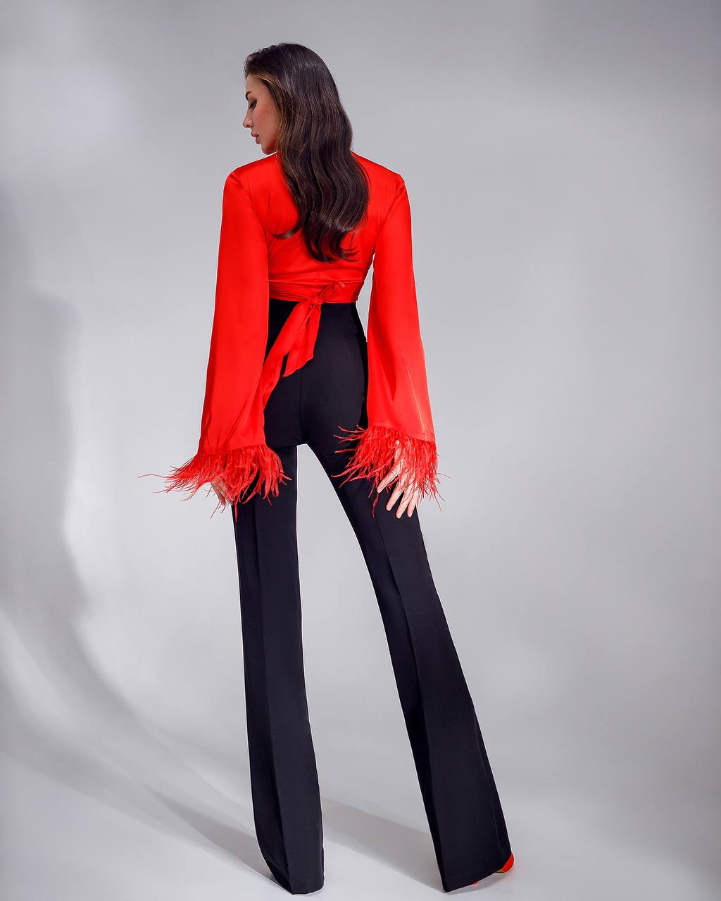 Woman wearing a red blouse with fringe details and black pants on a gray background