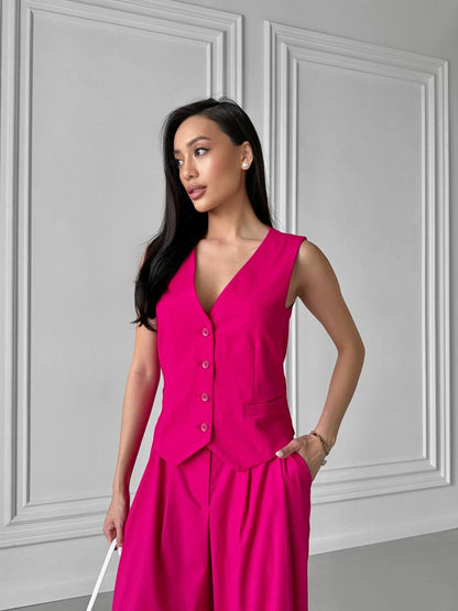 Woman wearing a bright pink sleeveless jumpsuit against a gray paneled wall.
