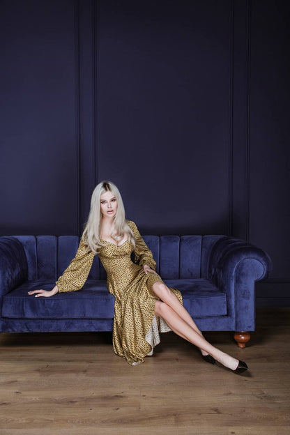 Woman in a gold dress sitting on a blue couch against a dark purple wall.