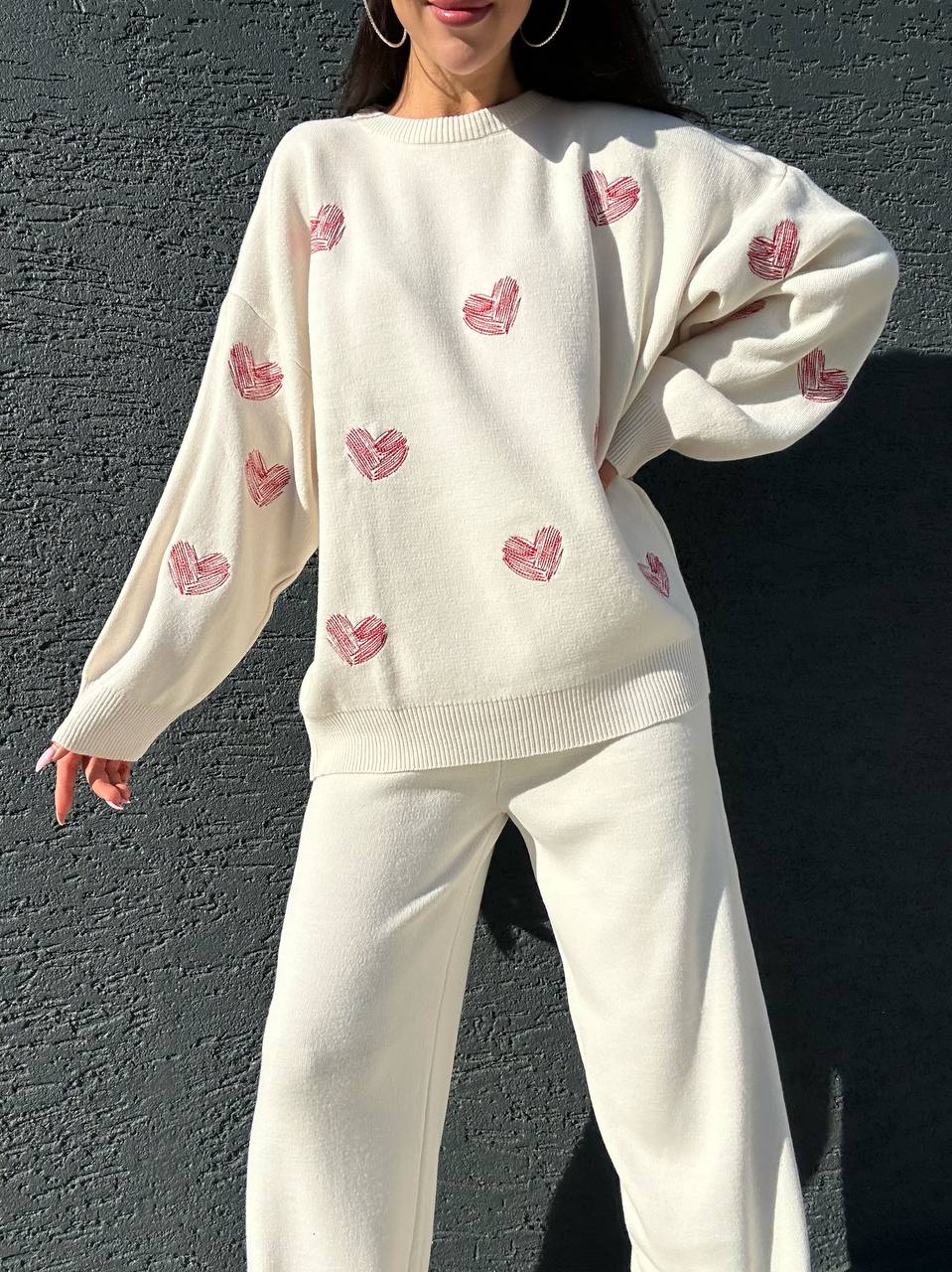 Person wearing a cream-colored sweater with pink heart patterns against a dark background