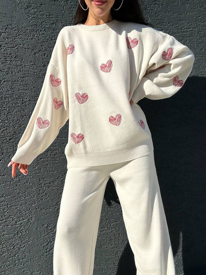 Person wearing a cream-colored sweater with pink heart patterns against a dark background