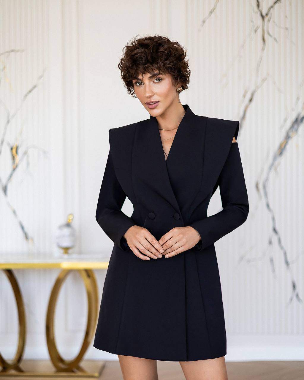 Woman wearing a black coat against a marble wall background