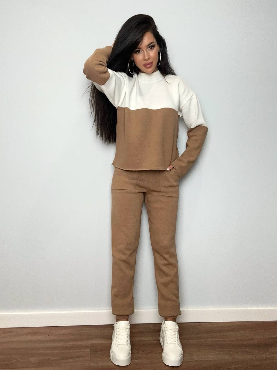 Woman wearing a brown and white outfit against a light gray wall.