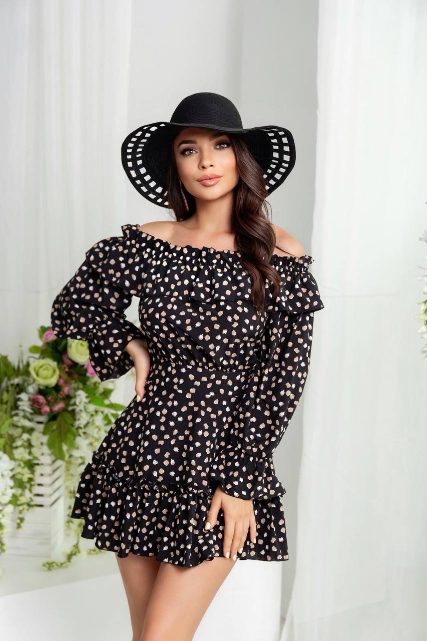 Woman wearing a black polka dot dress and black hat against a white curtain background