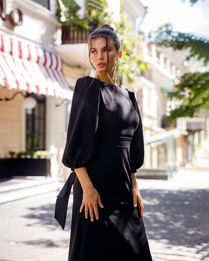 Woman in a black dress standing on a street with buildings and trees in the background