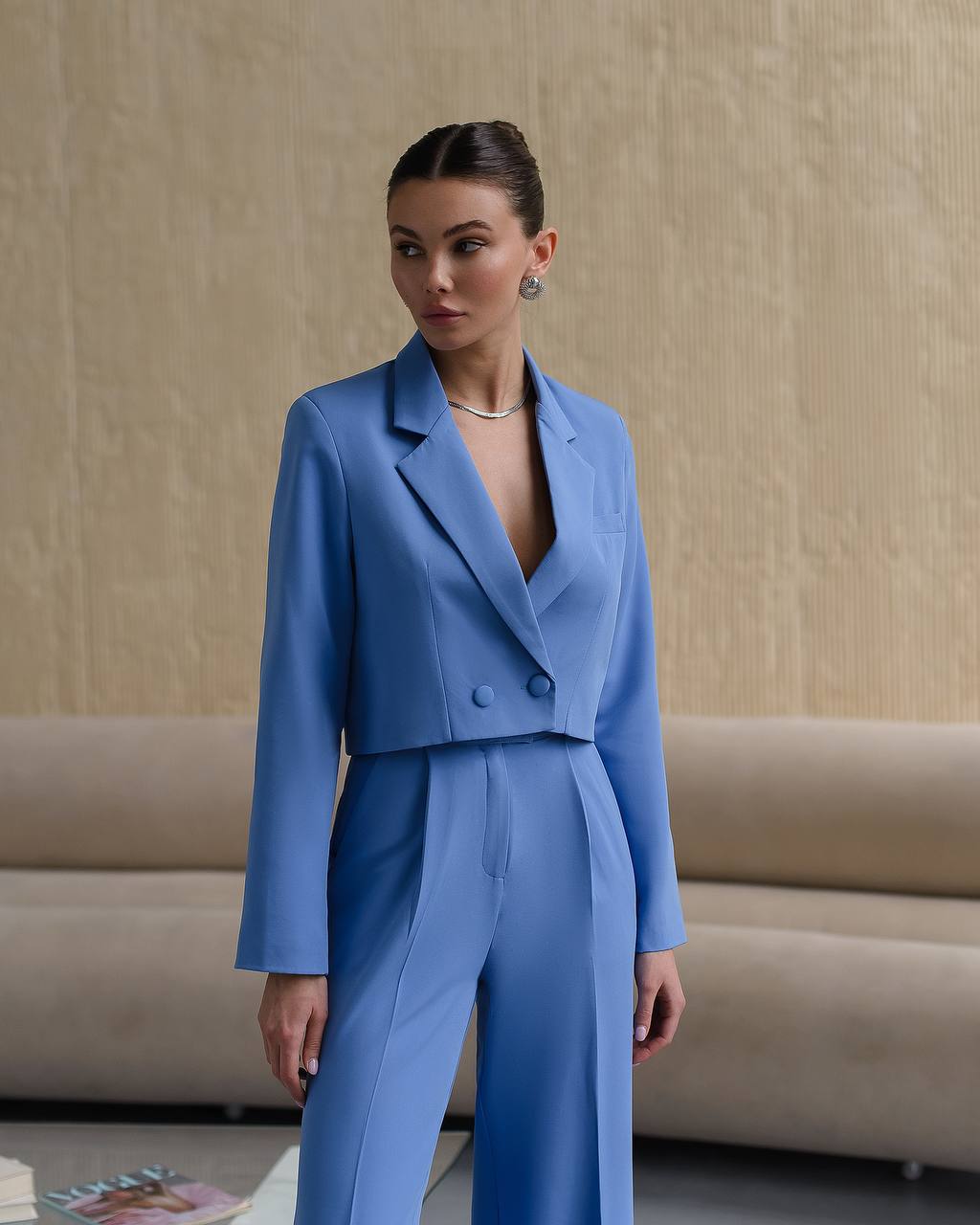 Woman wearing a blue suit standing against a beige wall.