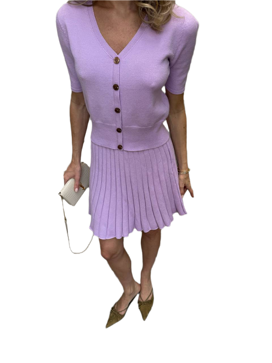 Woman wearing a light purple outfit with a cardigan and pleated skirt on a white background