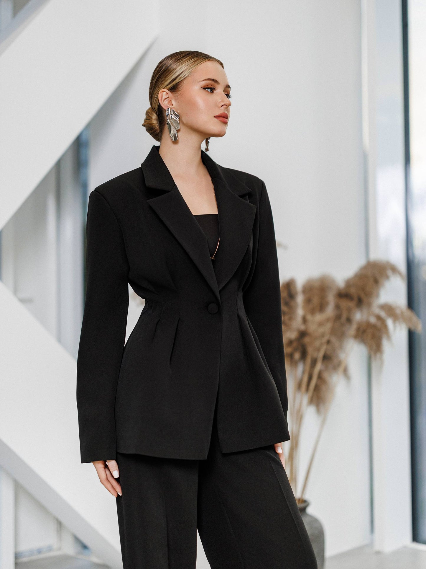Woman wearing a black suit standing in an indoor setting with a neutral background