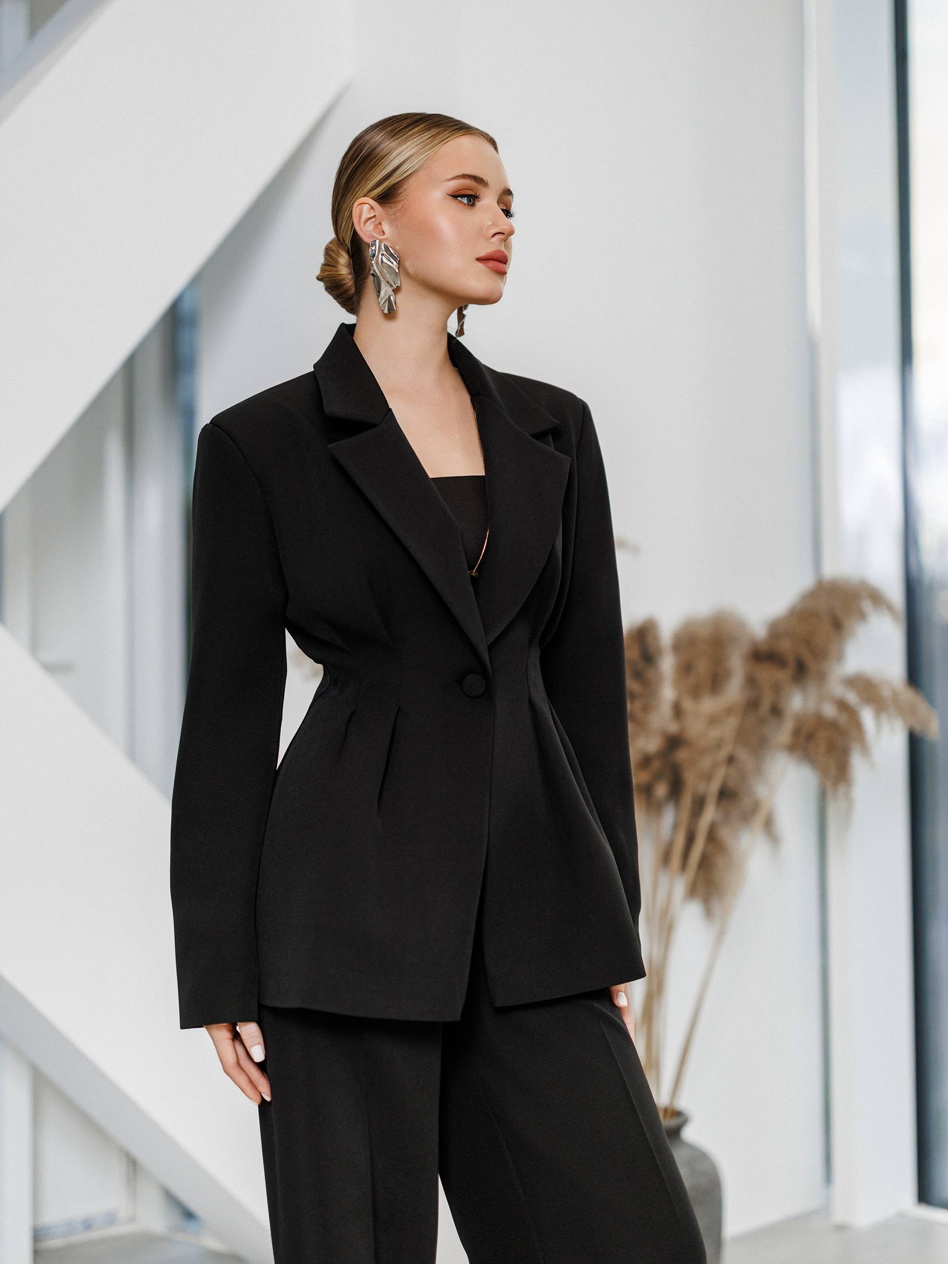 Woman wearing a black suit standing in an indoor setting with a neutral background