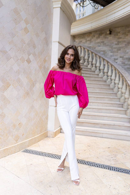 Woman in a bright pink top and white pants standing in a marble staircase.
